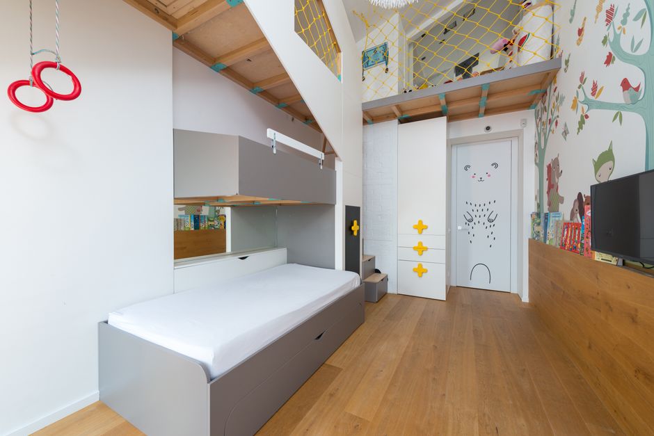 A compact interior room featuring a top bunk bed with a wooden frame and ladder, positioned against the right wall, which is covered with exposed brickwork. The lower part of the bunk includes a works